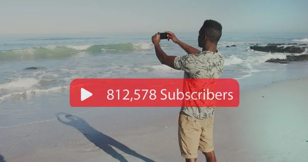 Image of speech bubble with subscribers and numbers over man filming sea with smartphone. digital interface, social media and global networking concept digitally generated image.