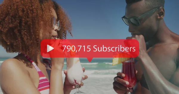 Image of speech bubble with subscribers numbers over couple having drinks on beach. digital interface, social media and global networking concept digitally generated image.