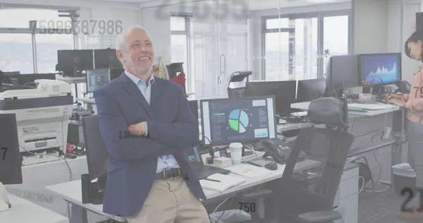 Image of numbers floating, a happy man standing in an office. Digital interface and global business, digitally generated image