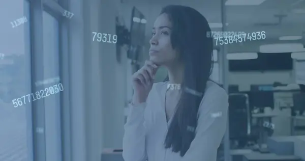 Image of digital interface showing floating numbers and a woman looking through window in an office. Digital interface and global business, digitally generated image