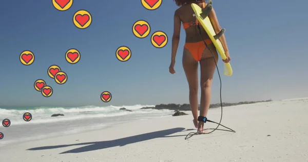 ビーチでサーフボードを運ぶ女性の上の心臓デジタルアイコンのイメージ デジタルインターフェース ソーシャルメディア グローバルテクノロジーコンセプトをデジタルで生成 — ストック写真