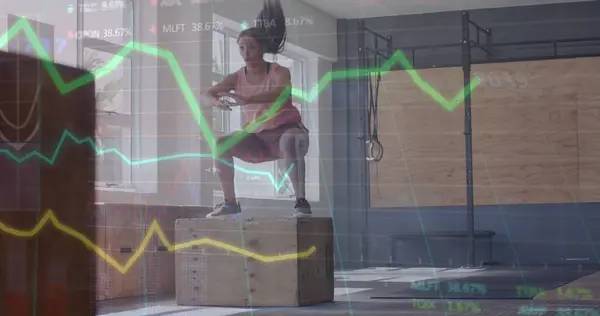 Image of graph processing data over caucasian woman jumping on box cross training at gym. Fitness, exercise, strength, data, digital interface and technology digitally generated image.