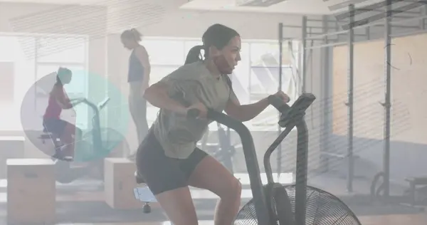 Image of data processing on interface over caucasian woman cross training on elliptical at gym. Fitness, exercise, strength, data, digital interface and technology digitally generated image.
