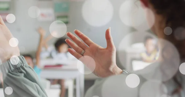 stock image Image of white bokeh spots over hands of diverse female teacher and pupils in class. Communication, teaching, school, education, childhood and learning, digitally generated image.