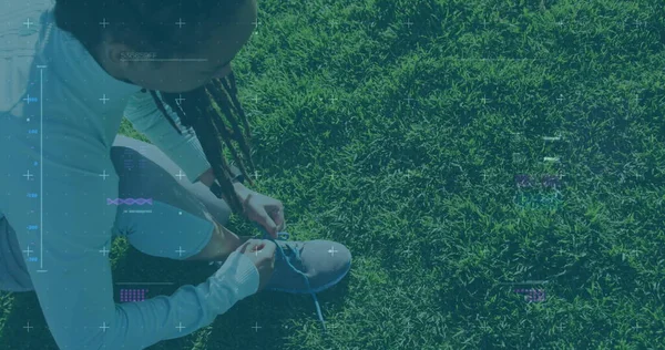 Image of statistics and graphs over woman tying her shoes on grass. Digital interface global sport and performance concept digitallygenerated image.