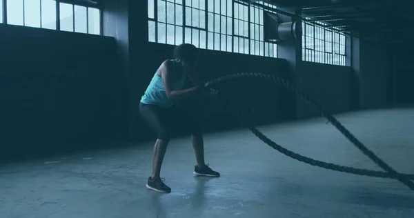 Image of shining light floating over woman exercising with ropes in an abandoned building. Digital interface global sport and performance concept digitally generated image.