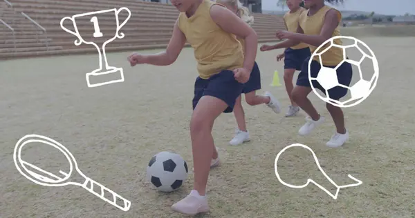Image of sports icons over happy diverse schoolgirls playing football on sports field. Sports, health, school, education, childhood and friendship, digitally generated image.