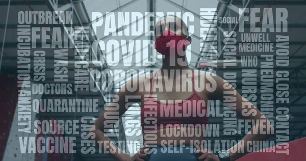 Coronavirus concept texts against african american woman woman wearing face mask standing in the gym. coronavirus covid-19 pandemic and fitness concept