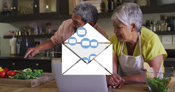 Image of envelope mail icons over senior couple using laptop at home. digital interface, social media, connection and communication concept digitally generated image.
