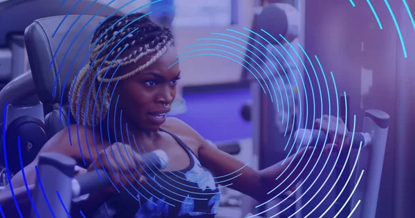Image of blue line spiral rotating over african american woman exercising at gym. sport and competition concept, digitally generated image.
