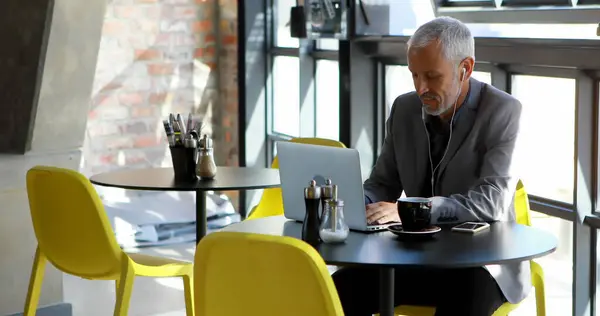 Caucasian businessman works on his laptop at a cafe. He is focused on his task in a casual office setting.