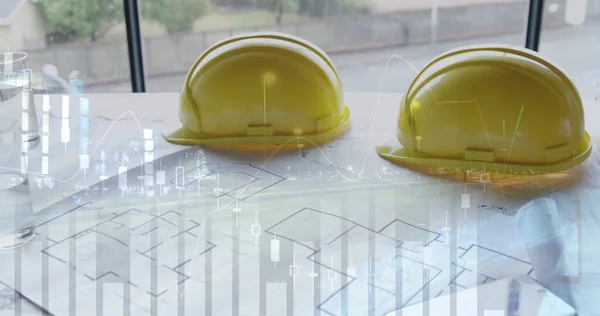 Safety hats on building plans laid out on a table.