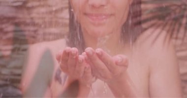 Çift ırklı mutlu bir kadının duşta yüzüne sıçrayan palmiye yapraklarının animasyonu. Doğa, kendine bakım, güzellik, rahatlama, refah ve yaşam tarzı, dijital olarak üretilen video.