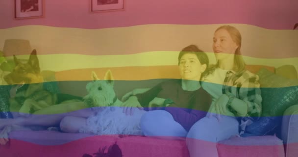 在快乐的高加索女同性恋夫妇和宠物狗一起在沙发上放松时 为他们的骄傲彩虹旗帜的动画 家庭生活 Lgbtq 同性恋 骄傲和生活方式 数码视频 — 图库视频影像