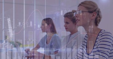 Beyaz kadınlar ofis ortamındaki bir ekrandaki verileri analiz ederler. İş stratejilerinin bir parçası olarak dikkatle mali eğilimlere odaklanırlar.