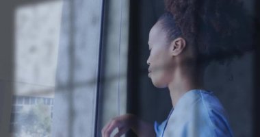 Pencereden dışarı bakan mutsuz Afro-Amerikan kadın doktor üzerine yağmur animasyonu. Üzüntü, iş, stres, depresyon, sağlık hizmetleri ve akıl sağlığı, dijital olarak üretilen video.