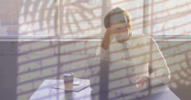 Ofis masasında dizüstü bilgisayar kullanan yorgun Kafkas işadamının penceresine yağmur yağması. İş, aşırı çalışma, stres, fazla mesai ve yorgunluk, dijital olarak oluşturulmuş video.