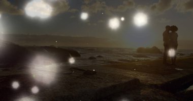 Kayaların üzerinde birlikte duran Afrikalı Amerikalı çifte karşı süzülen parlak ışık noktaları. Aşk ve ilişki kavramı