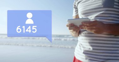 Kumsalda telefonuyla yazı yazarken beyaz bir adamın fotoğrafını çek. Adamın yanında bir mesaj baloncuğunun dijital görüntüsü var. Bir takip simgesi ve bir sayı sayımı var.