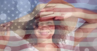 Güneşli plajda gülümseyen güneş şapkalı kadın üzerinde hafif noktalar ve Amerikan bayrağı. Amerika, yaz, tatiller, sağlıklı yaşam tarzı, kutlama ve vatanseverlik, dijital olarak üretilen video.