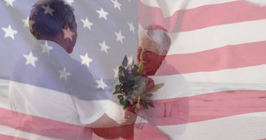 Amerika Birleşik Devletleri 'nin bayrağı sahilde çiçekli yaşlı melez bir çiftin üzerinde. Amerikan vatanseverliği, çeşitlilik ve gelenek kavramı dijital olarak oluşturuldu.