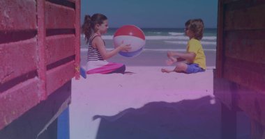 Pink and blue light trails against caucasian brother and sister playing with beach ball at the beach. national siblings day awareness concept
