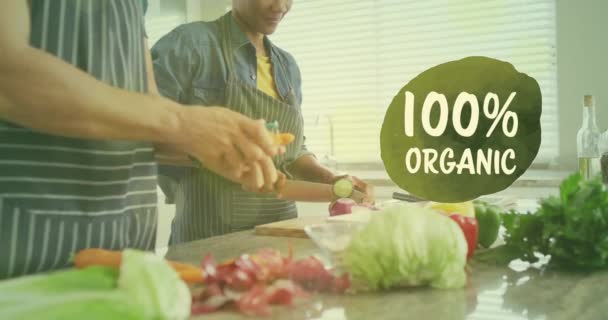 キッチンで健康的な食事を準備する多様なカップルを超えた100 オーガニックテキストのアニメーション 有機食品 健康的な食事 調理コンセプトデジタル生成されたビデオ — ストック動画