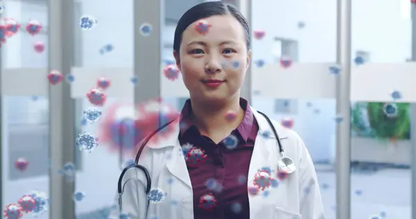 Image of macro Covid-19 cells floating on a view of an Asian female doctor wearing a lab coat and smiling background. Coronavirus Covid-19 pandemic concept digital composite.