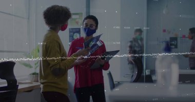 Data processing over two diverse female office colleagues wearing face masks discussing at office. Business data and analytics concept