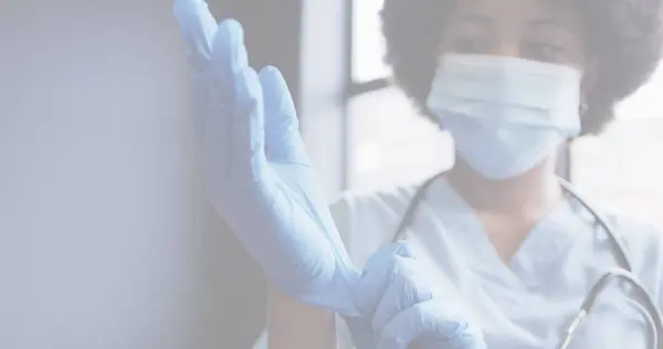 Image of covid 19 cells with female doctor wearing mask putting on gloves. healthcare and protection during coronavirus covid 19 pandemic, digitally generated image.