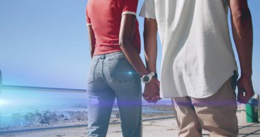 Sahilde el ele tutuşan bir çiftin ortasında hareket eden ışığın görüntüsü. Tatiller, aktif yaşam tarzı ve pozitiflik kavramı dijital olarak oluşturuldu.