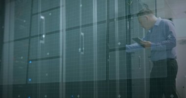 Beyaz adam ofisteki bir sunucu odasında verileri inceliyor. Ağ güvenliği veya donanım sorunlarını sürdürmeye odaklanmış durumda.