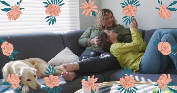 图片上的粉色花朵在快乐的高加索女同性恋夫妇放松在沙发上使用智能手机 融合和幸福概念数字生成的图像 — 图库照片