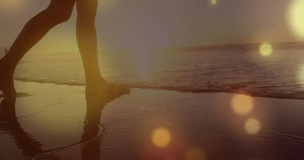Glowing yellow spots of light against mid section of a woman walking on the beach. Love and relationship concept
