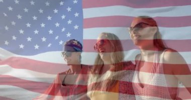 Neşeli beyaz kadın arkadaşlarının güneşli sahilde yürümesi üzerine Amerikan bayrağının animasyonu. Amerika, yaz, tatiller, dostluk, rahatlama, yaşam tarzı ve vatanseverlik, dijital olarak üretilen video.