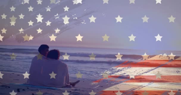 ラグで包まれた幸せな多様なカップルの上のアメリカの旗のアニメーションは 日没のビーチに座りました アメリカ ロマンス お祝い 愛国心 デジタル生成されたビデオ — ストック動画