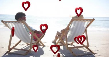 Yaz aylarında kumsaldaki şezlonglarda birbirine aşık çift üzerinde hareket eden kalplerin animasyonu. Aşk, romantizm, sevgililer günü ve tatil konsepti, dijital olarak oluşturulmuş video.