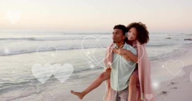 Yaz aylarında kumsalda kadınları sırtında taşıyan melez bir adamın üzerinde hareket eden kalp animasyonu. Aşk, romantizm, sevgililer günü ve tatil konsepti, dijital olarak oluşturulmuş video.