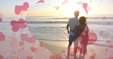 Yaz aylarında kumsalda birbirine sarılan farklı çiftlerin üzerinde hareket eden kalplerin animasyonu. Aşk, romantizm, sevgililer günü ve tatil konsepti, dijital olarak oluşturulmuş video.
