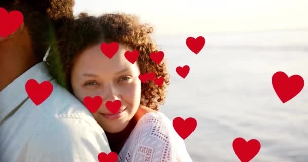 夏にビーチで抱擁する愛の多様なカップルの上に移動する心のアニメーション ロマンス バレンタインの日と休暇の概念 デジタル生成されたビデオ — ストック動画