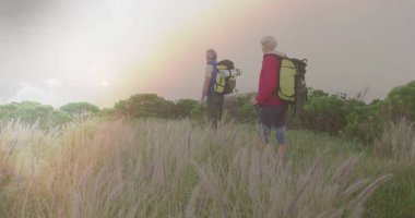 Kafkasyalı yaşlı çift hızlı hareket eden bulutlar ve gün batımında kırsalda yürüyüş yapıyor. aktif yaşam tarzı, sağlıklı emeklilik ve özgürlük konsepti, dijital olarak oluşturulmuş görüntü.