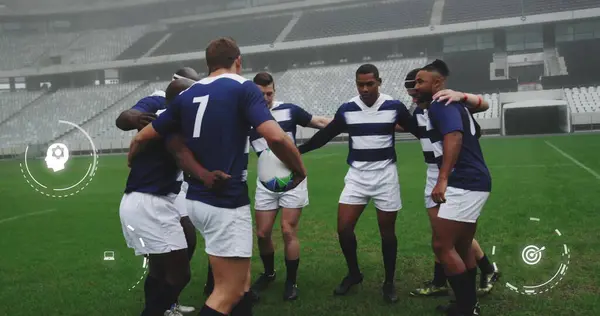 Image of media icons over diverse male rugby team in huddle at stadium. Sport, team, competition, social network, digital interface, internet and communication, digitally generated image.