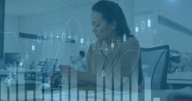 Asyalı bir kadın, orta yaşlı, açık mavi tişört giyiyor, bilgisayardaki verileri analiz ediyor. Ekrana odaklanmış, ofis ortamında özenle çalışıyor.