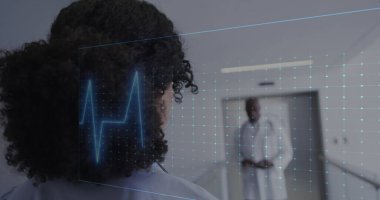 Kıvırcık saçlı melez kadın Afrikalı Amerikalı doktora bakıyor. Her ikisi de dijital ekranlar tarafından izlenen hastanedeki sağlığı tartışıyor.