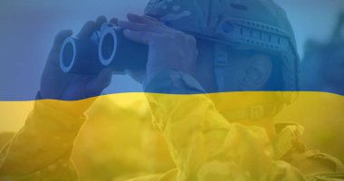 Ukrayna bayrağı ve ellerinde dürbünle kask takan beyaz bir profesyonel. Kamuflaj üniforması giymiş, kısa kahverengi saçlı.