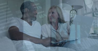 Evdeki yatakta dizüstü bilgisayar kullanarak mutlu çiftin üzerinde hareket eden bilgi arayüzü görüntüsü. Dijital kompozit, iş dünyası, rapor, grafik, aşk, birlikte, rahatla, teknoloji ve yaşam tarzı konsepti.