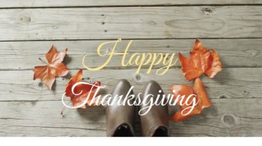 Sonbahar yaprakları ve ahşap arka planda ayakkabılar üzerindeki mutlu şükran günü metninin animasyonu. Amerikan geleneği, şenlik, kutlama ve gelenek konsepti dijital olarak oluşturulmuş video.