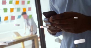 Akıllı telefon kullanan Afro-Amerikan iş adamının üzerinde numarası olan sosyal medya simgelerinin animasyonu. Küresel iletişim, sosyal medya, bağlantılar ve dijital arayüz konsepti dijital olarak oluşturulmuş video.