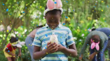 Paskalya yumurtası avında çocuklarla birlikte paskalya yumurtası tutan Afrikalı Amerikalı bir çocuk üzerinde konfeti animasyonu. Paskalya, gelenek, din ve inanç konsepti dijital olarak oluşturulmuş video.