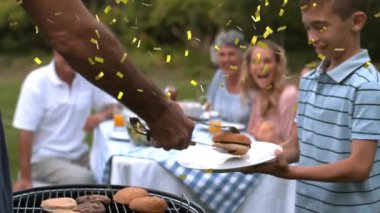 Aile içi konfeti animasyonu açık havada mangal yaparken elinde hamburger tutan bir çocukla. Kutlama, piknik, yaz, kaynaşma, neşe, ızgara